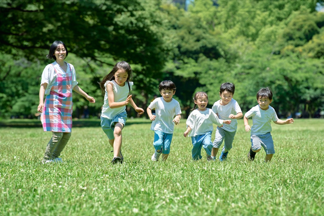 緑地でかけっこをする子どもたちと見守るスタッフ